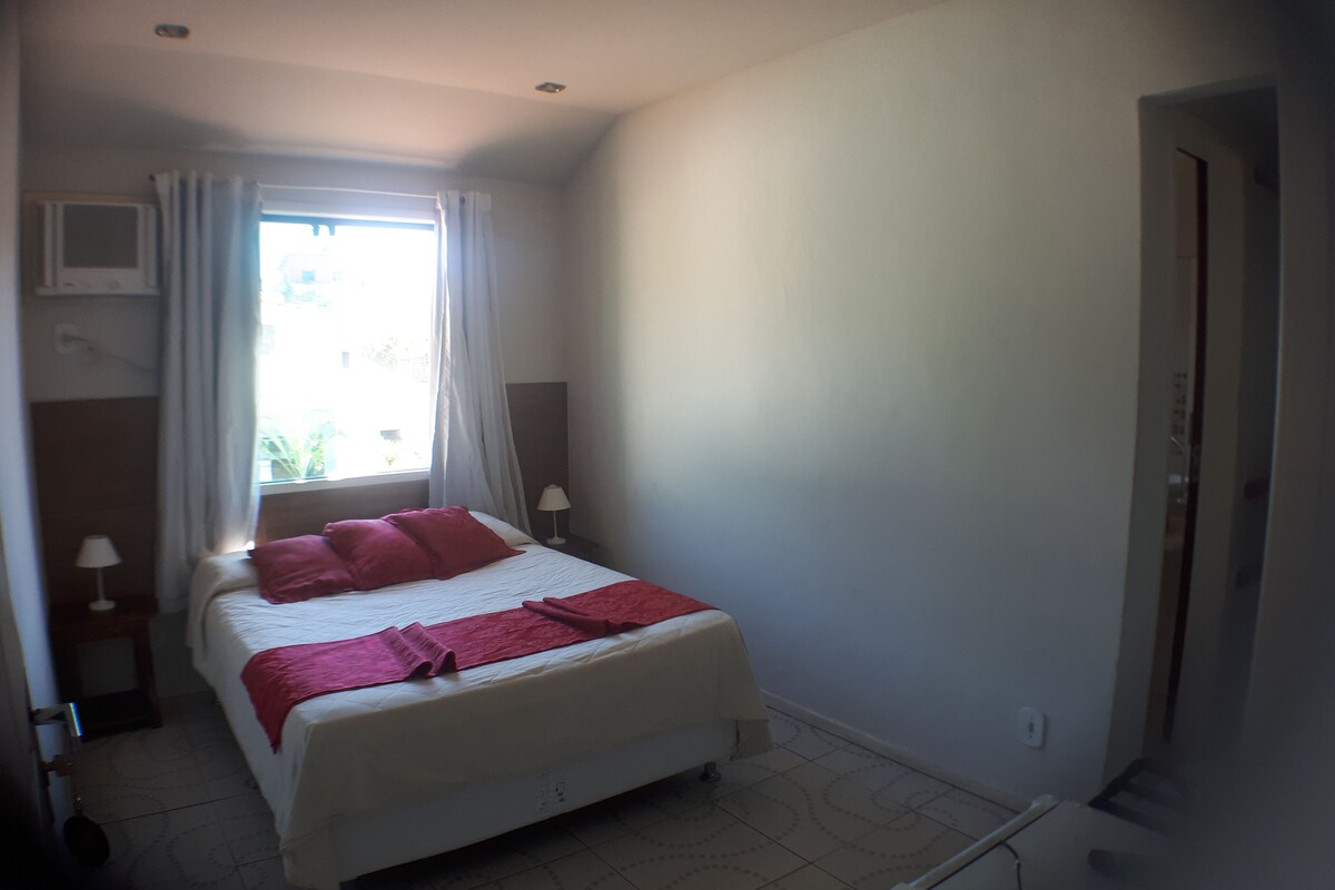 A bedroom with a bed, a window with curtains, a bedside lamp, and a radiator.