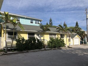 A two-story yellow building with a flat roof, surrounded by palm trees and a small garden. - Beach View, Private Plunge Pool, Charming 1938 Bungalow Madeira Beach Gulf-Blvd (Madeira Beach)