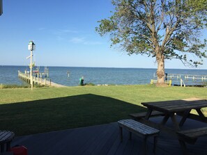 A wooden deck with picnic tables, a grassy area, a tree, and a pier extending into the water.