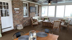 A cozy room with a brick wall, a white door, and a window. There is a table with chairs and a bench.