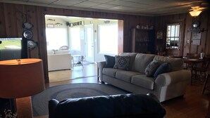 A cozy living room with a sofa, a cat tree, and a lamp. There is a dining area with a table and chairs.
