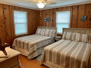 Une chambre avec deux lits, des murs en bois, un ventilateur de plafond et une table de chevet.