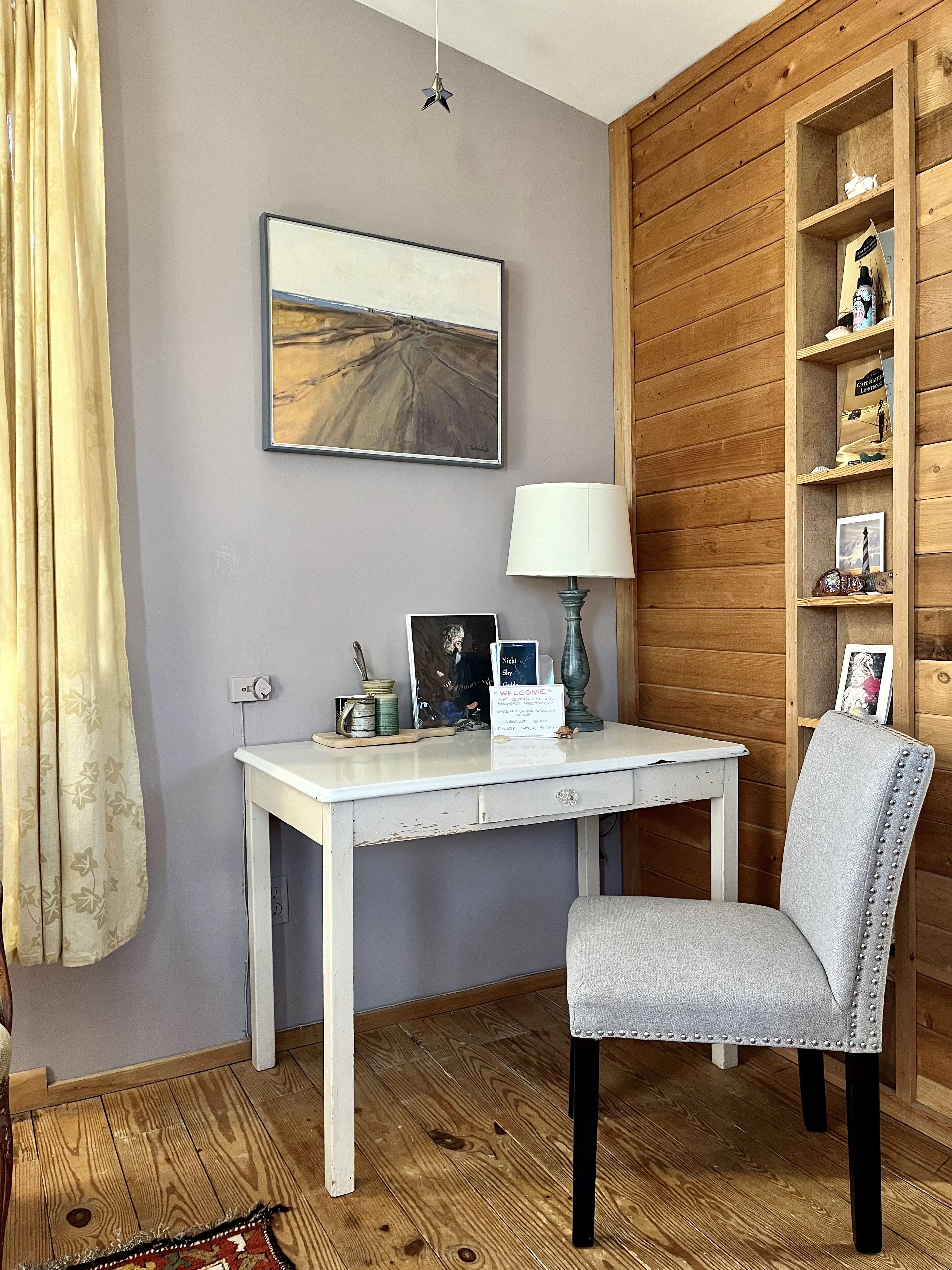 Une pièce avec un bureau blanc, une chaise grise, une bibliothèque en bois et un tableau accroché au mur.