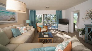A living room with a sofa, armchair, and TV, a balcony with curtains, and a painting on the wall. - Kingston Arms Paradise!
 Saint  Armands Circle & Lido Beach!  Fully Equipped! (Sarasota)
