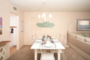 Un coin repas avec une table blanche dressée pour quatre personnes, un lustre et une œuvre d’art encadrée accrochée au mur.