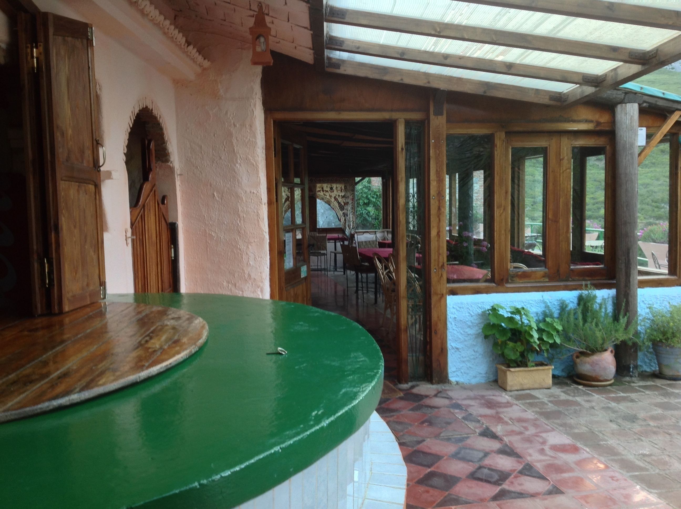 Un espacio exterior techado con un mostrador verde, puertas de madera y vistas a un comedor interior.