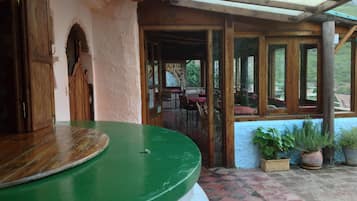 Un espacio exterior techado con un mostrador verde, puertas de madera y vistas a un comedor interior.