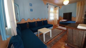 Un soggiorno con un divano blu, un tavolino da caffè bianco, un mobiletto in legno e un televisore.