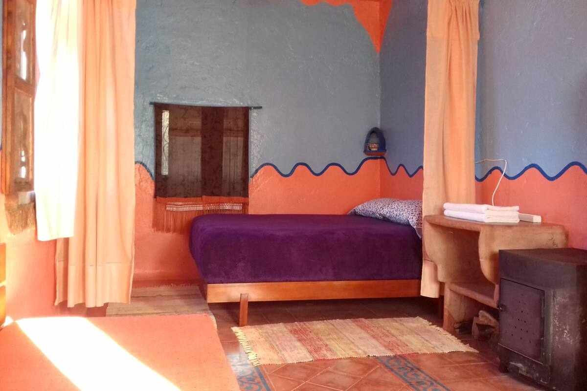 A room with a bed, a small table, a heater, and a window with curtains.