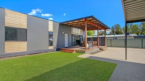 Una casa moderna con un porche cubierto, un césped bien cuidado y un patio trasero cercado.