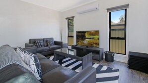 Una sala de estar moderna con un sofá, un televisor de pantalla plana y ventanas amplias.