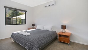 Un dormitorio con cama, mesita de noche, lámpara, aire acondicionado y ventana con persianas.