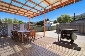 A covered patio with a wooden table and chairs, a barbecue grill, and a view of a house in the background. - Snowgum Bright Retreat - 2 (Bright)