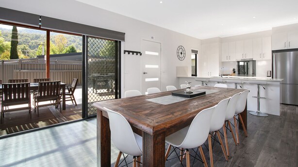 Una cocina moderna con armarios blancos, electrodomésticos de acero inoxidable y una mesa de comedor de madera con sillas blancas.