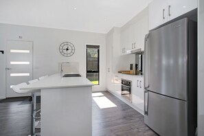 A modern kitchen with a central island, stainless steel appliances, and a clock on the wall. - Snowgum Bright Retreat - 2 (Bright)