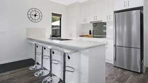 Una cocina moderna con armarios blancos, un refrigerador de acero inoxidable y una zona con taburete de bar.