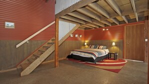 A bedroom with a bed, two bedside tables, a nightstand, a wooden staircase, and a door. - Studio @ Quins Gap Retreat (Bright)