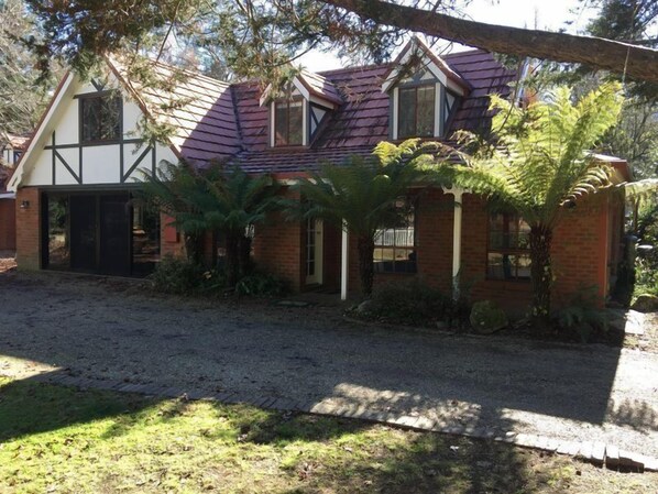 A two-story house with a mix of brick and timber framing, a gravel driveway, and surrounding greenery. - Tudor House - Large Family Home (Bright)
