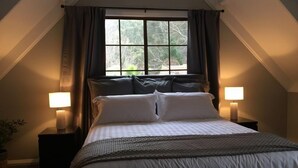 A bedroom with a large bed, two bedside lamps, a window with curtains, and a plant. - Tudor House - Large Family Home (Bright)