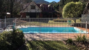 A residential property with a swimming pool, surrounded by a white fence, and a house with a gabled roof in the background. - Tudor House - Large Family Home (Bright)