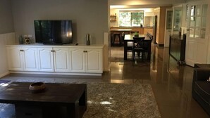 A spacious living area with a flat-screen TV, a coffee table, and a kitchen in the background. - Tudor House - Large Family Home (Bright)