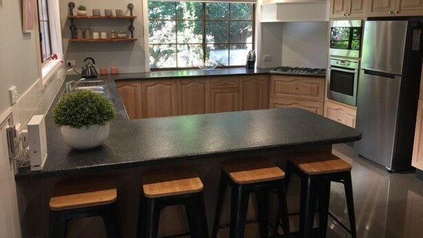A modern kitchen with a large island, bar stools, stainless steel appliances, and a window with a view of greenery. - Tudor House - Large Family Home (Bright)