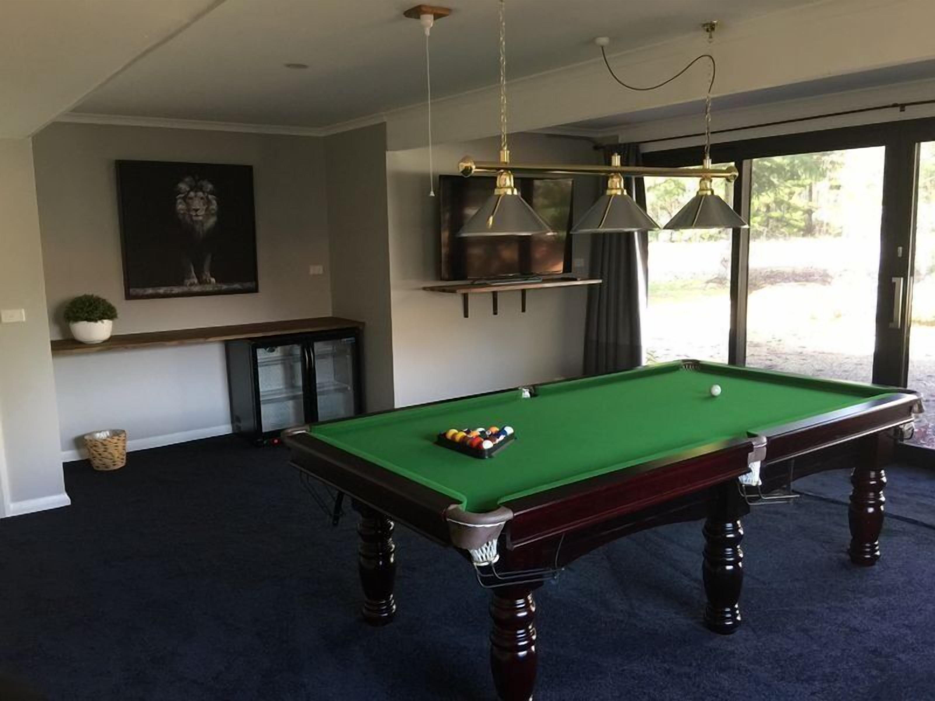 A pool table in a room with a dark carpet, a ceiling fan, and a large window.