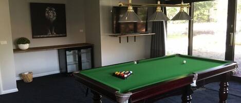 A pool table in a room with a dark carpet, a ceiling fan, and a large window.