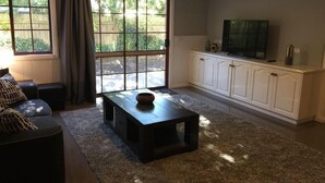 A living room with a sofa, a coffee table, a TV, and a sliding glass door leading to a backyard. - Tudor House - Large Family Home (Bright)