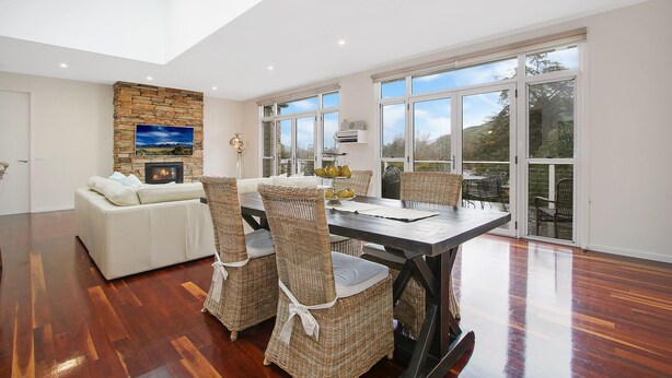 Amplia sala de estar con chimenea, una mesa de comedor con sillas y ventanas grandes que ofrecen vistas al exterior.