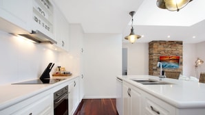 Una cocina moderna con armarios blancos, horno empotrado, pileta de acero inoxidable y una pared decorativa de piedra.