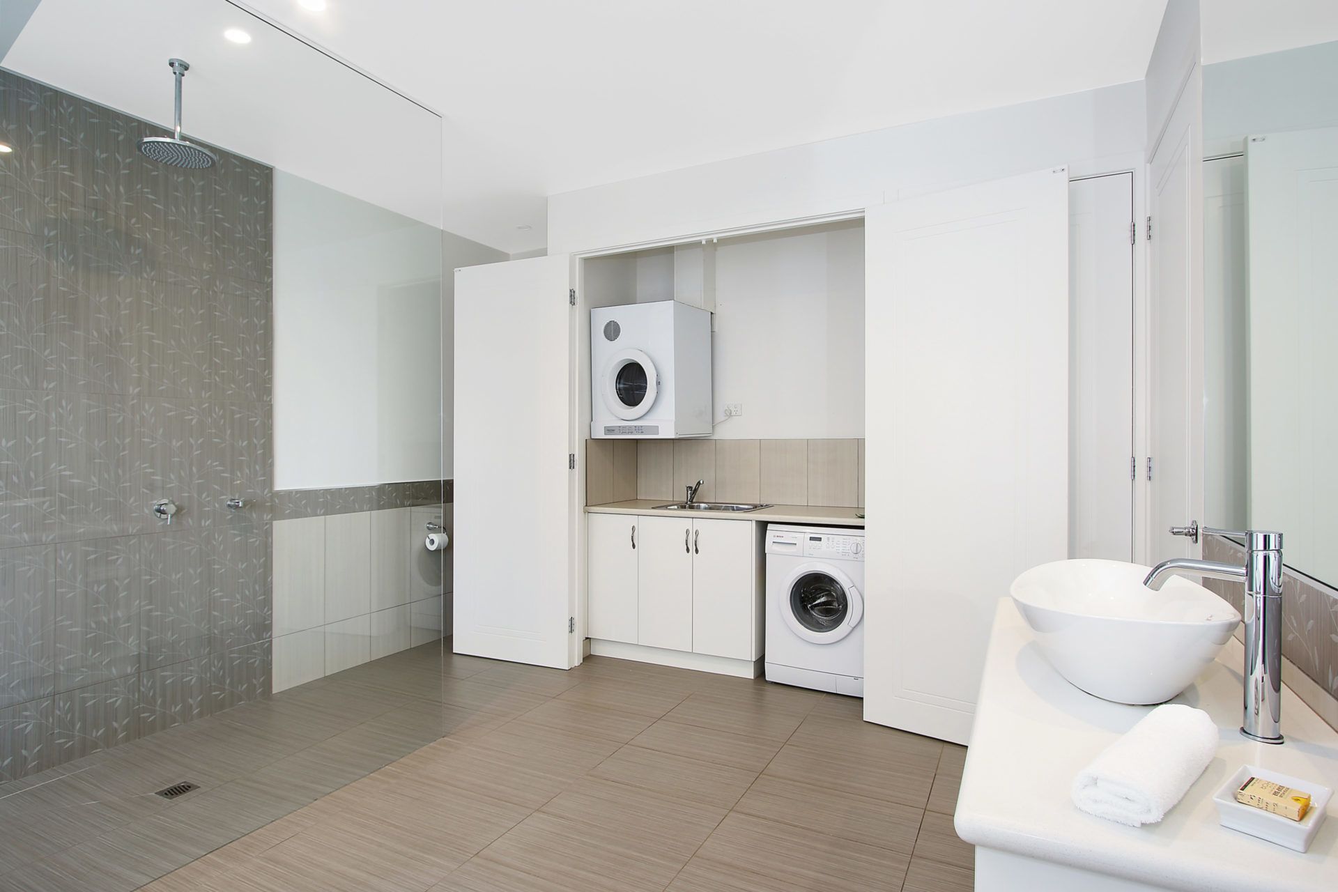A modern bathroom with a walk-in shower, a built-in washing machine, and a sink with a large mirror.