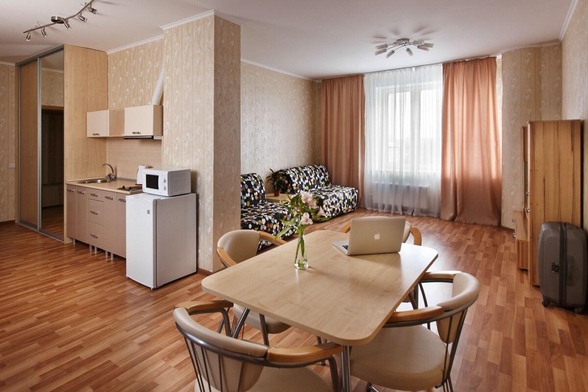 Un espacio habitable compacto con kitchenette, una zona de comedor con mesa y sillas, un sofá y una maleta.