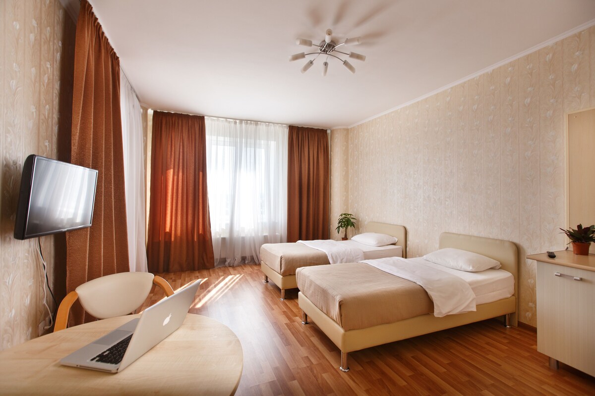 Habitación de hotel con dos camas, un escritorio con una computadora portátil, un televisor montado en la pared y un ventilador de techo.