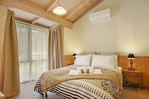 A hotel room with a wooden ceiling, a bed with a striped bedspread, two bedside tables with lamps, and an air conditioning unit on the wall.