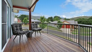 A wooden deck with two cushioned chairs and a small table, overlooking a residential area with houses and hills. - 3 Peaks Rise - BRIGHT (Bright)