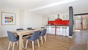 A modern kitchen with a red backsplash, wooden bar stools, and a dining area with a table and chairs. - 3 Peaks Rise - BRIGHT (Bright)