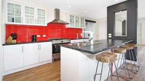 A modern kitchen with white cabinets, red tiles, a stove, and a large island with bar stools. - 3 Peaks Rise - BRIGHT (Bright)