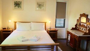 Une chambre d’hôtel comprenant un lit, deux tables de chevet, un bureau avec une chaise, un miroir et deux tableaux encadrés accrochés au mur.