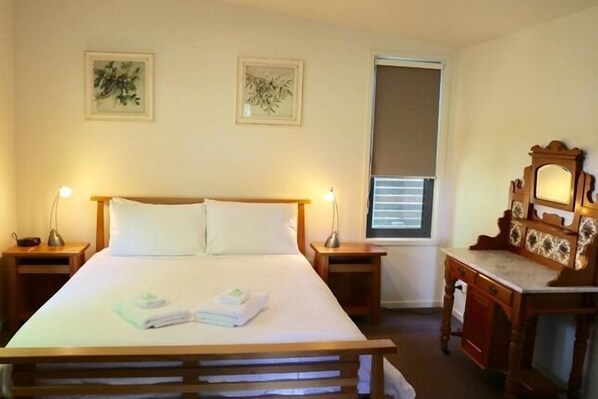 A hotel room with a bed, two bedside tables, a desk with a chair, a mirror, and two framed pictures on the wall. - Bright Woodlands Retreat (Bright)