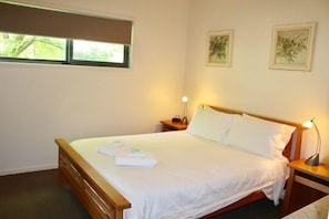 A neatly made bed with white linens and a wooden headboard, a bedside lamp, and two framed botanical prints on the wall. - Bright Woodlands Retreat (Bright)