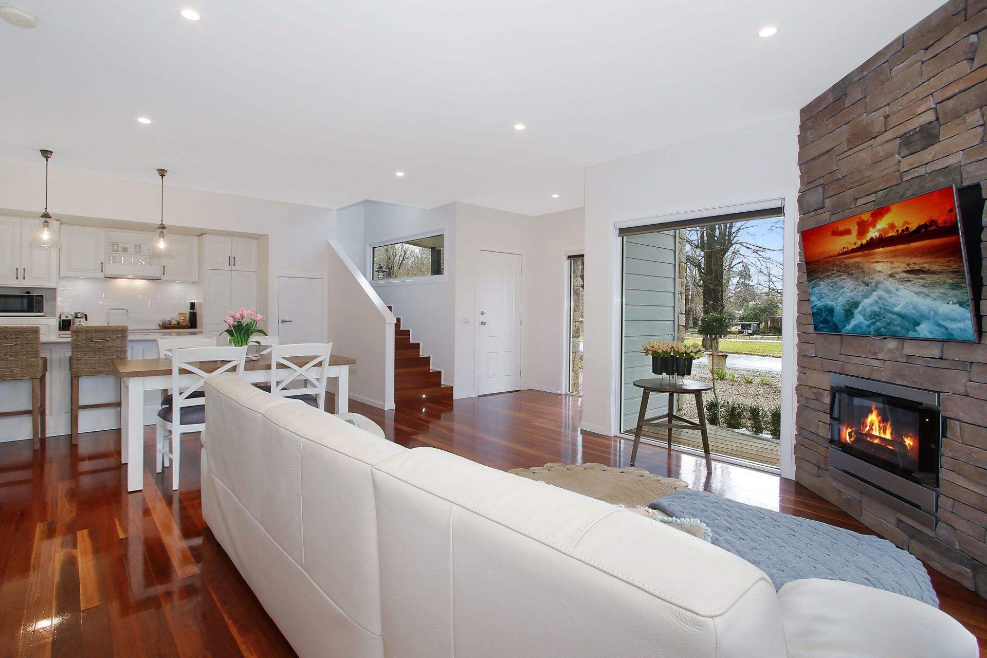 A modern living room with a white sofa, a fireplace, and a TV mounted on the wall.