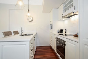 Una cocina compacta con muebles blancos, horno integrado, microondas y cafetera.
