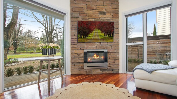 A living room with a stone fireplace, a large window, and a view of a garden. - Beyond Bliss - Guesthouse 2 (Bright)
