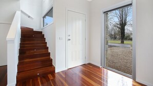 A modern interior with a wooden staircase, a white door, and a large sliding glass door leading to an outdoor area. - Beyond Bliss - Guesthouse 2 (Bright)