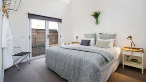 A bedroom with a bed, bedside tables, a lamp, a window with a view, and a towel rack. - Beyond Bliss - Guesthouse 2 (Bright)