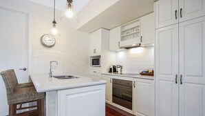 A modern kitchen with white cabinetry, a built-in microwave, a coffee maker, and a clock on the wall. - Beyond Bliss - Guesthouse 2 (Bright)
