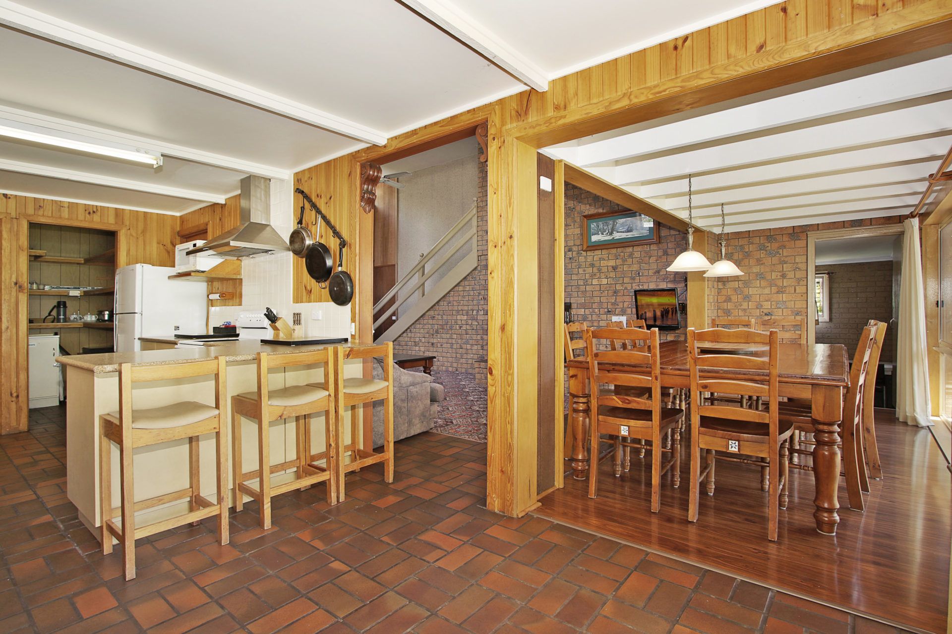 A spacious kitchen with wooden cabinets, a dining area with a large wooden table and chairs, and a brick wall with a fireplace.