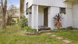 A white building with a front porch, a small garden, and a large plant. - Le Chateau - Centrally located (Bright)