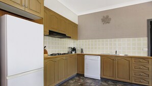 A kitchen with wooden cabinets, a white refrigerator, a dishwasher, and a tiled backsplash. - Le Chateau - Centrally located (Bright)